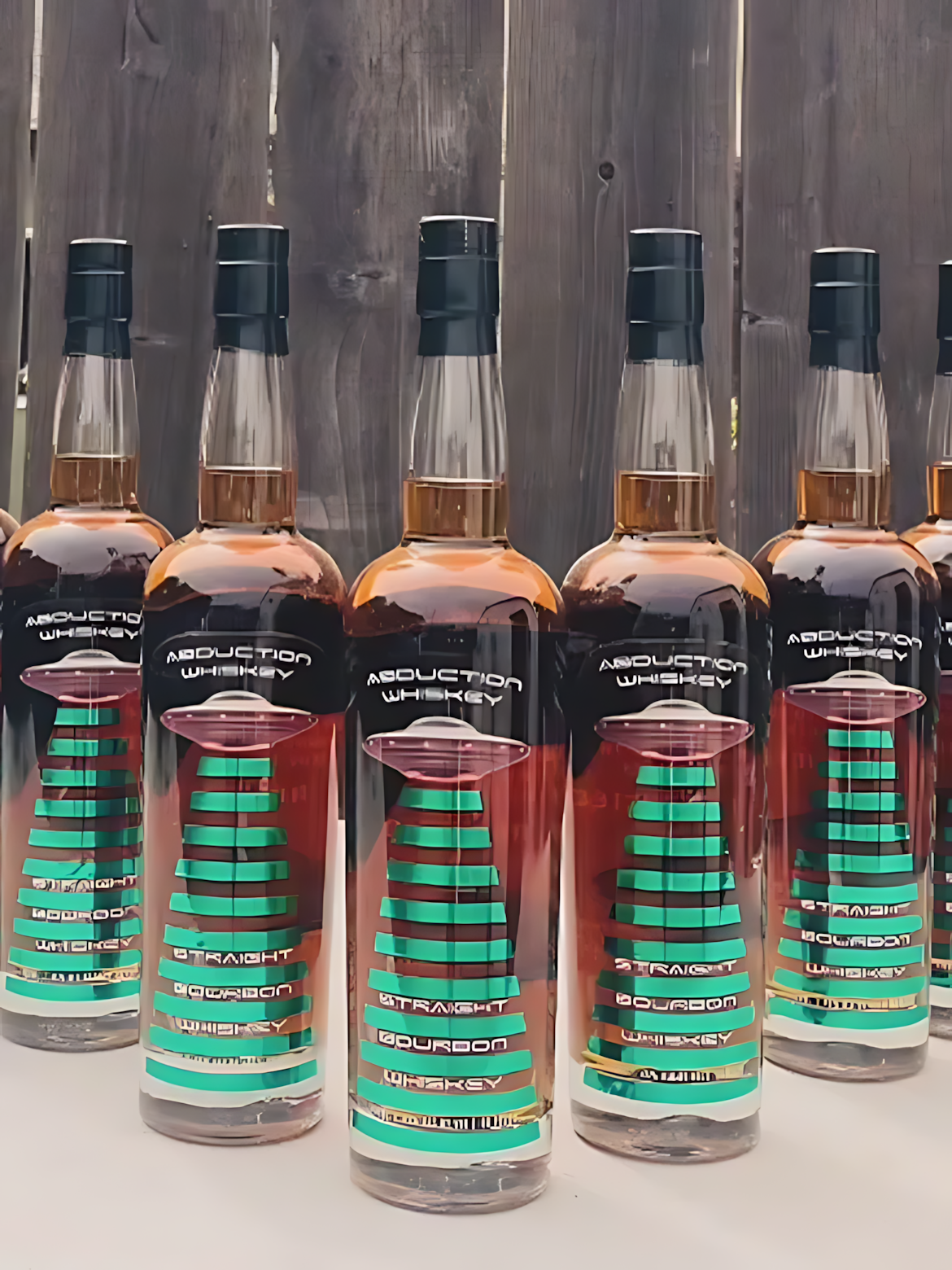 Row of Abduction Whiskey bottles lined up against a weathered fence
